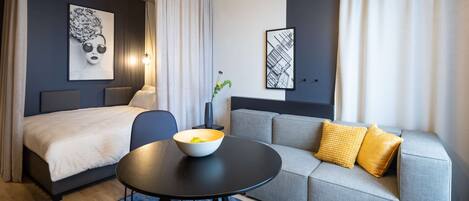 Una habitación de hotel moderna con una cama, un sofá, una mesa redonda con un cuenco y un jarrón con una planta.