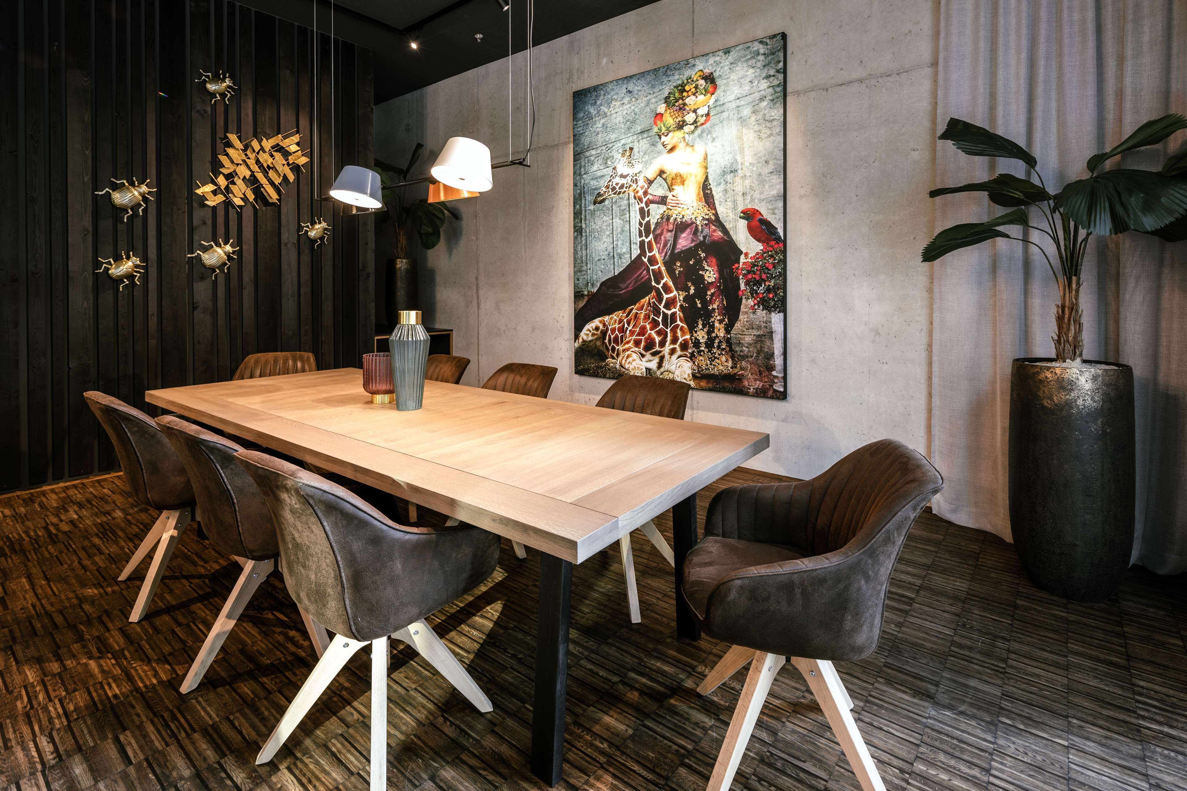 A modern dining area with a wooden table, leather chairs, a large painting, and a potted plant.