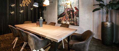 A modern dining area with a wooden table, leather chairs, a large painting, and a potted plant.
