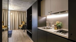 A modern kitchen with a built-in stove, a sink, and a cabinet. There is a chair and a small table in the adjacent living area. - Adina Serviced Apartments Vienna (Vienna)