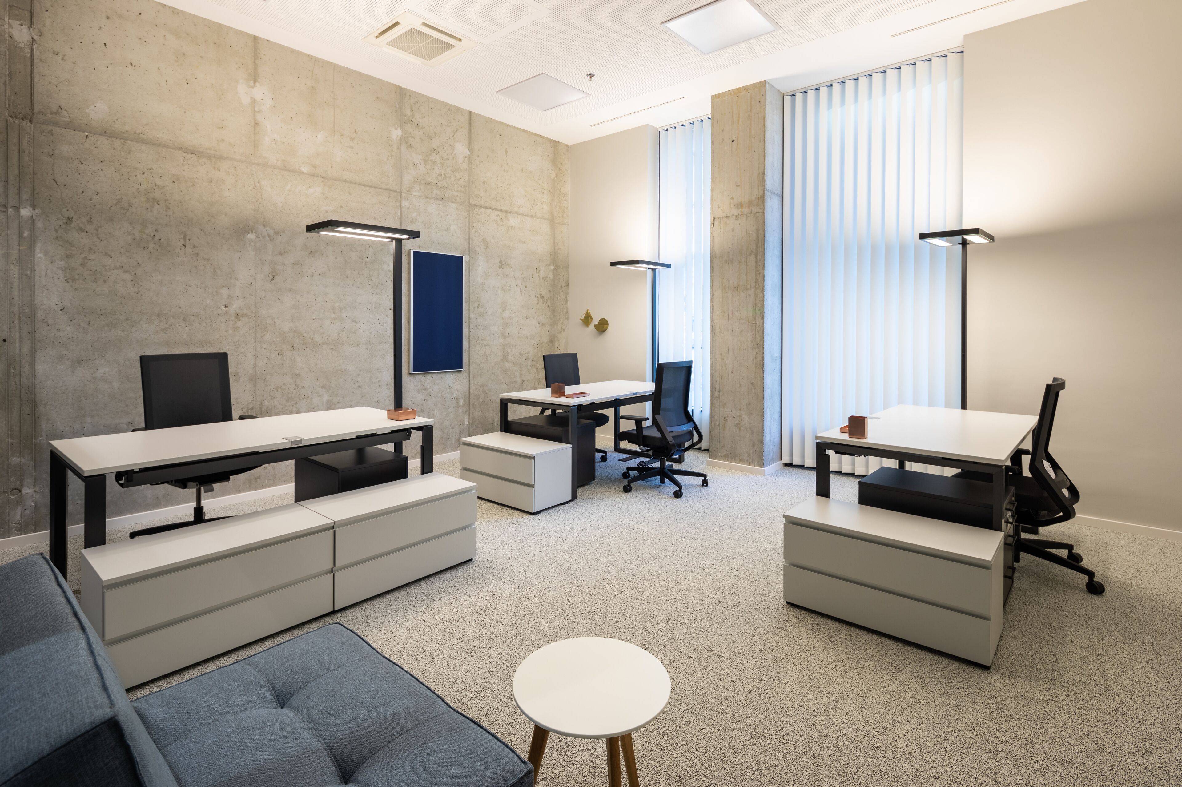 A modern office space with a large desk, office chairs, a sofa, and a small table.