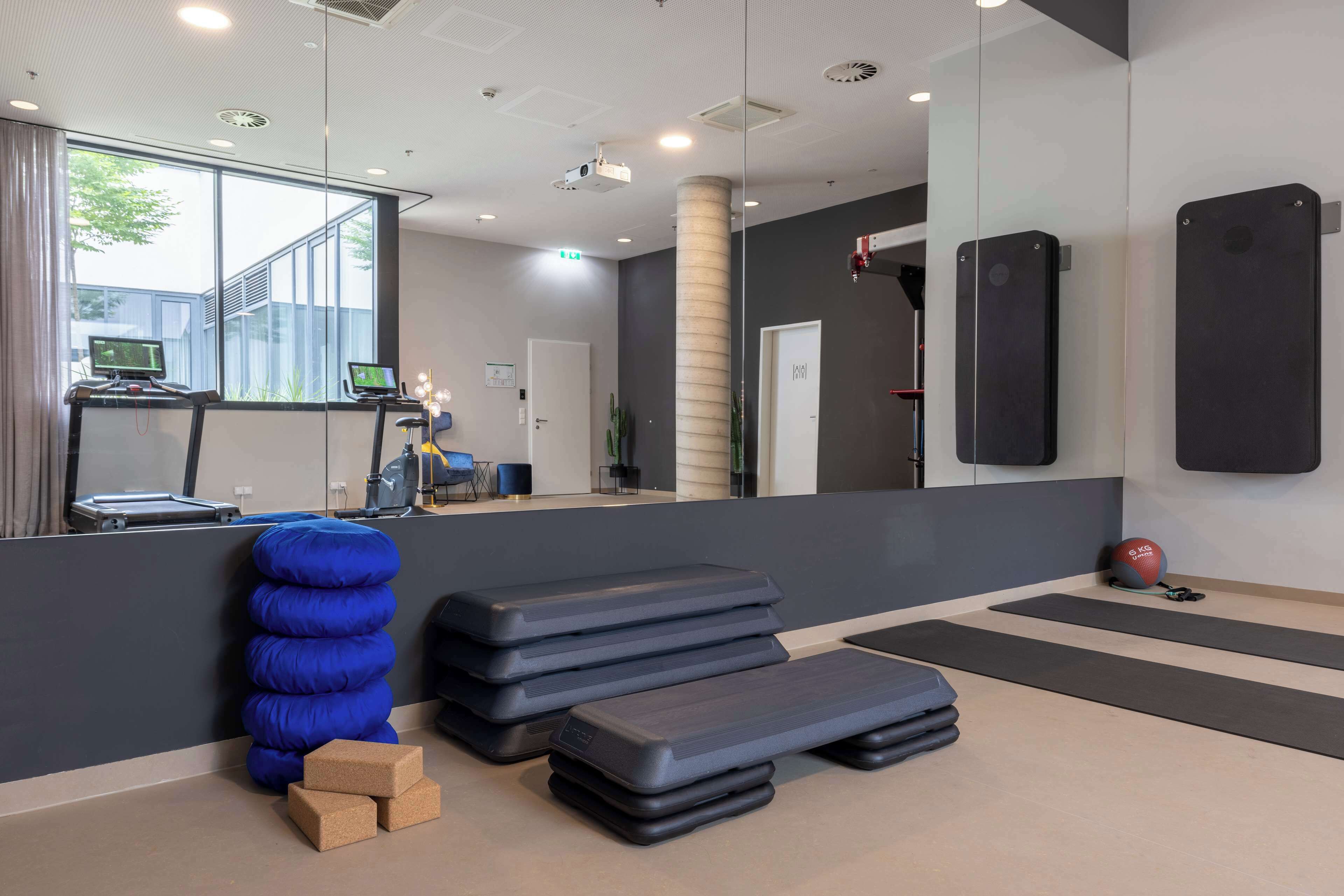 Un centre de remise en forme moderne, équipé de matériel d’exercice, doté d’un grand miroir et offrant une vue sur l’extérieur.