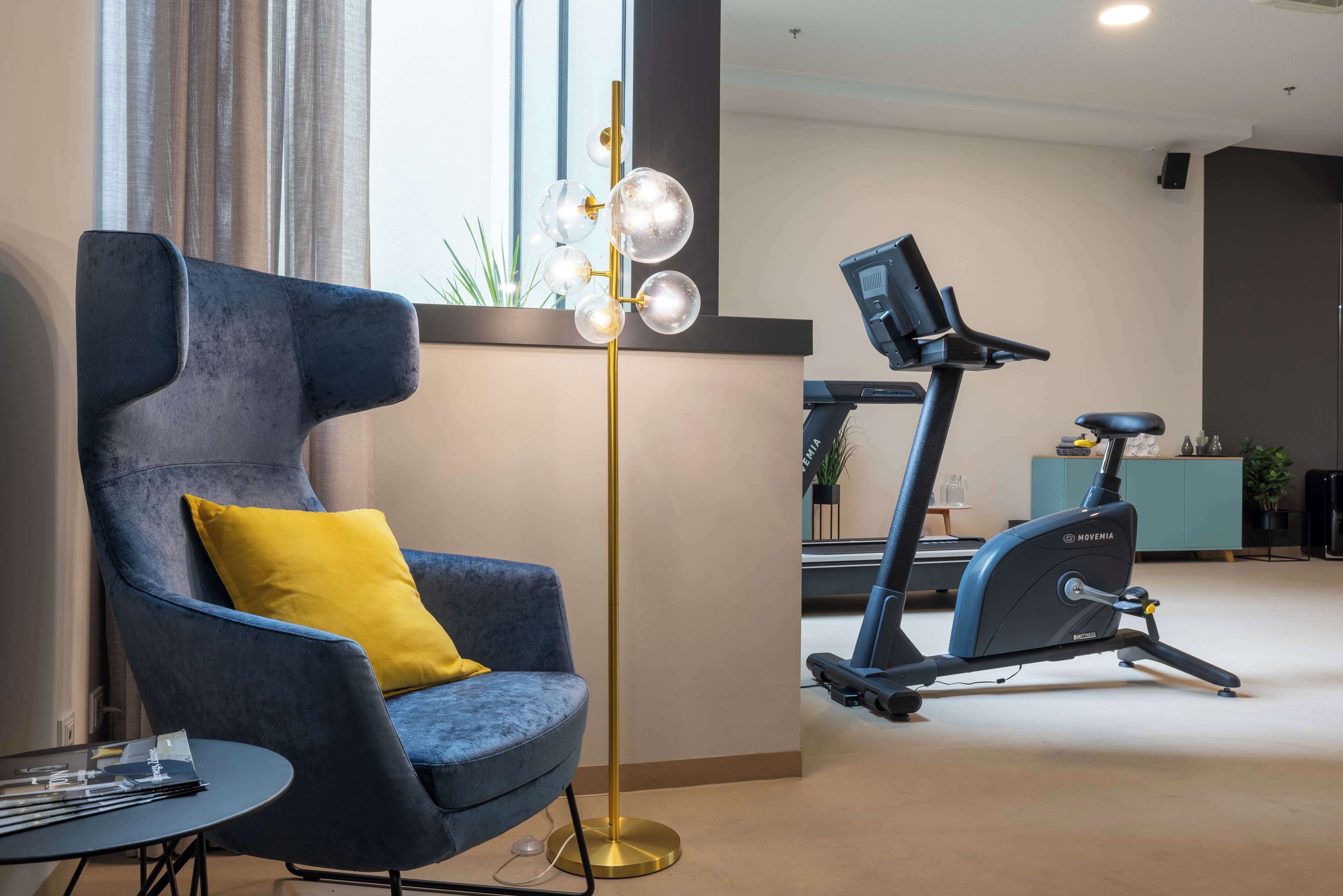 Et moderne værelse med en blå lænestol, en gulvlampe og en motionscykel.