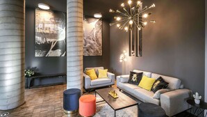 A modern living room with a grey sofa, orange ottomans, a coffee table, and a unique ceiling light fixture. - Adina Serviced Apartments Vienna (Vienna)