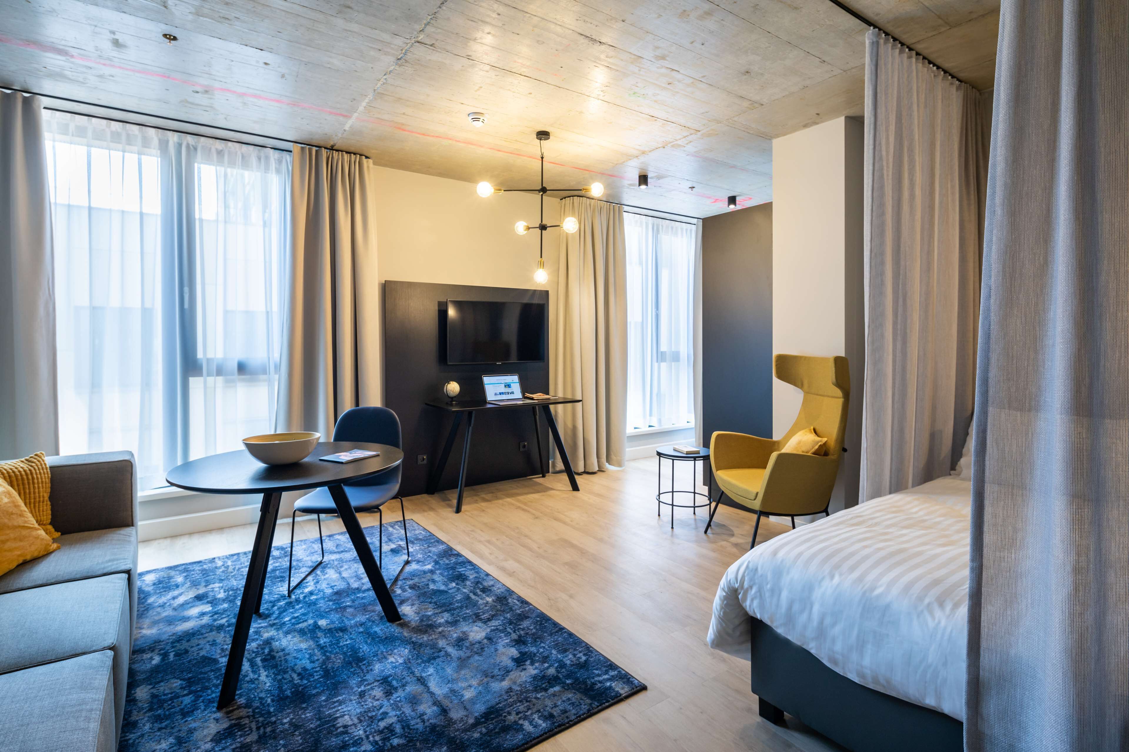 A modern hotel room with a bed, a desk, a TV, and a sofa.