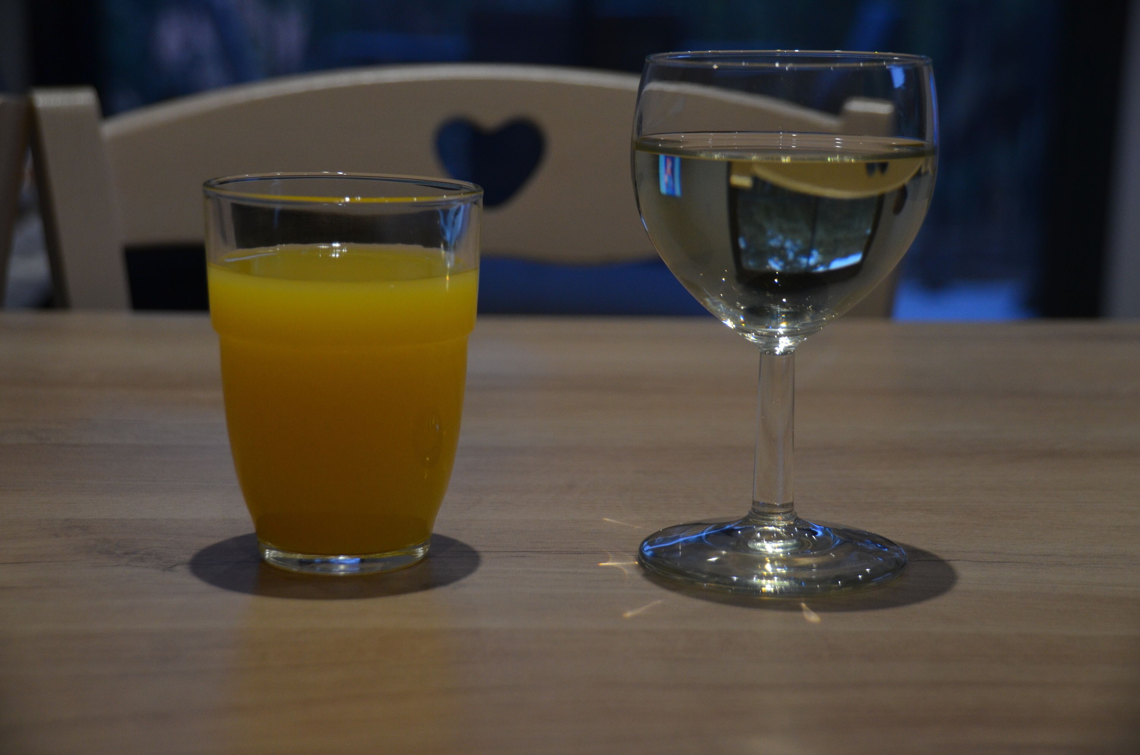 A table with two glasses, one containing orange juice and the other with water, on a wooden surface.