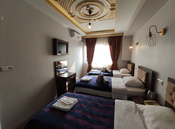 A hotel room with two beds, a TV, a desk, and a ceiling with decorative patterns.