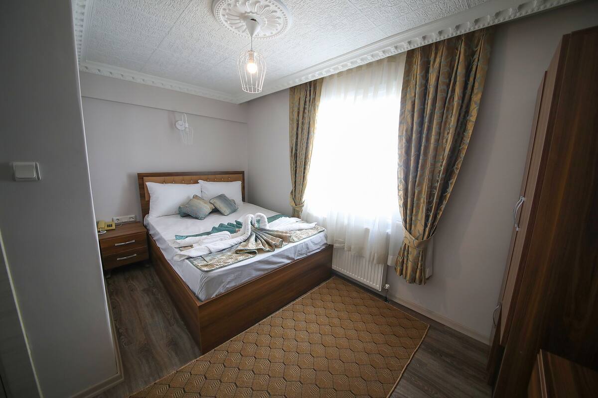 A bedroom with a wooden bed, a nightstand, a bedside table, a patterned rug, and a ceiling fan.