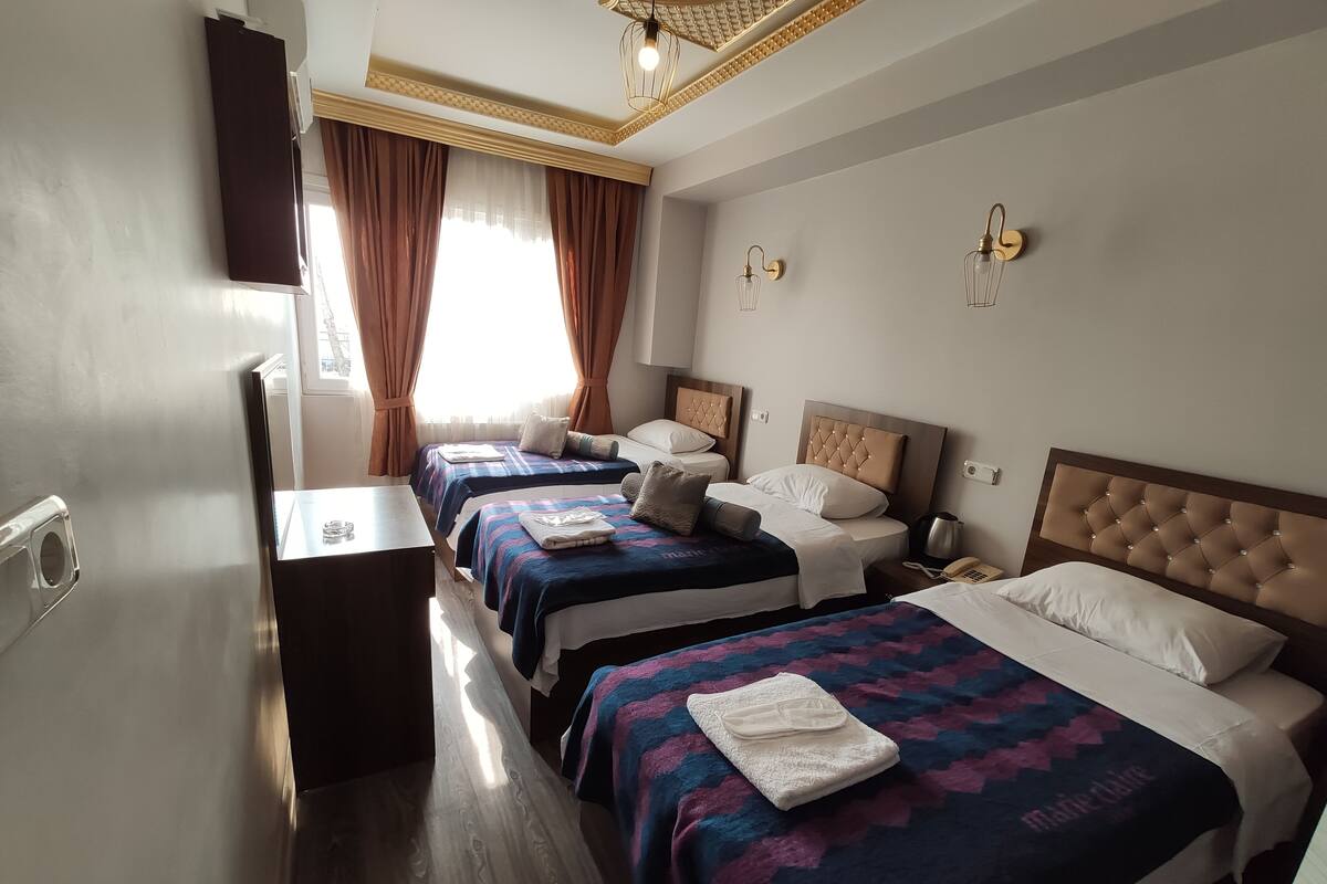 A hotel room with three beds, a desk, and a window with curtains.