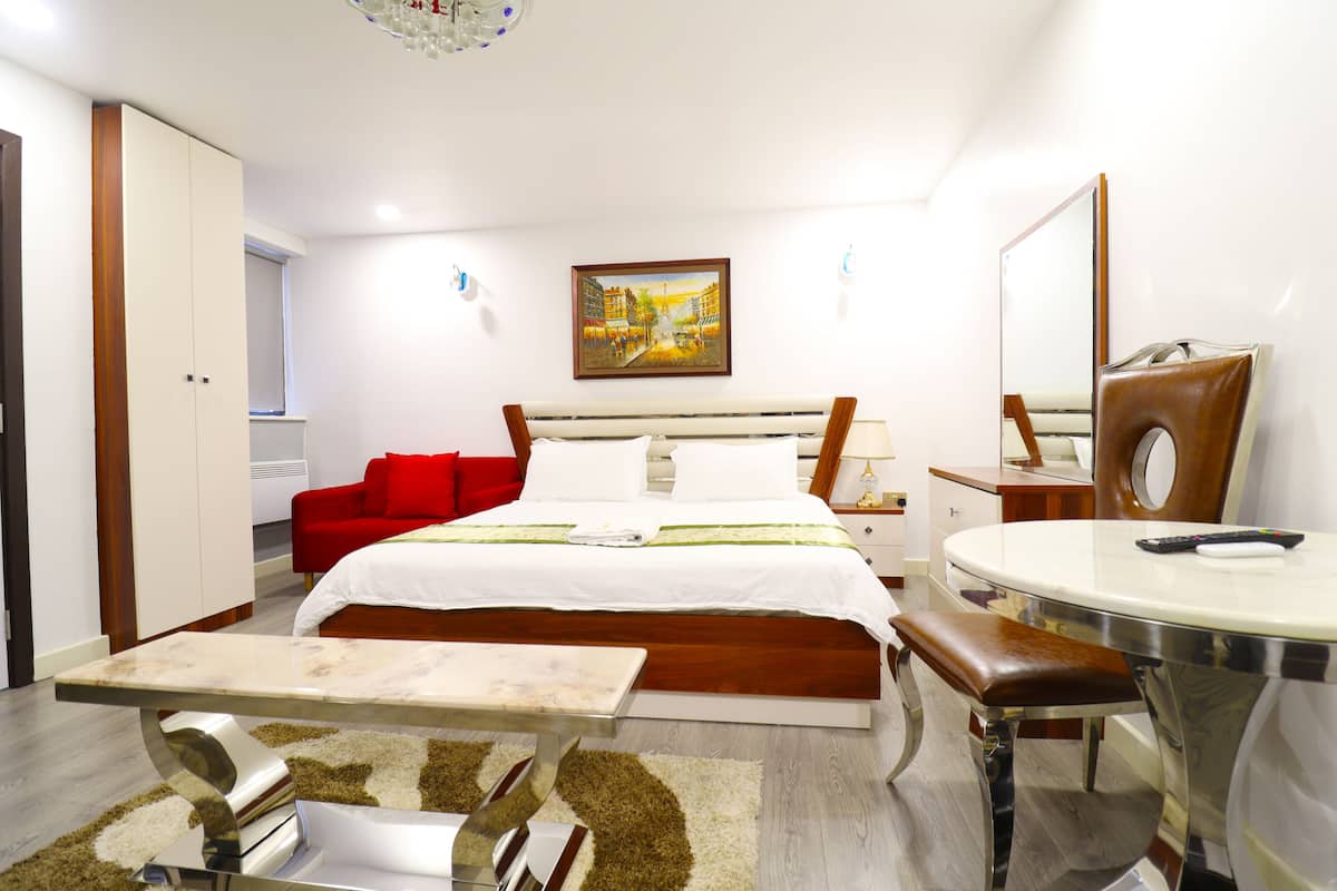Quarto de hotel com uma cama, um sofá vermelho, uma mesa de jantar e um espelho.