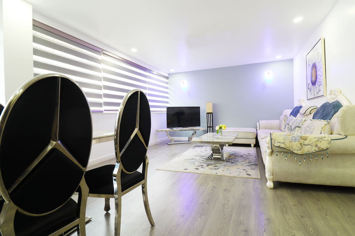 Uma sala de estar moderna com um sofá, duas cadeiras pretas, uma mesa de centro e uma televisão de tela plana.