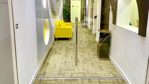 A modern hotel corridor with a patterned carpet, a yellow sofa, and a glass elevator. - Queen Stay Apartments (Sheffield)