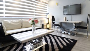 A modern living room with a sofa, a coffee table, a TV, and a dining area with chairs and a table. - Queen Stay Apartments (Sheffield)