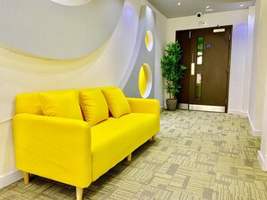 Un sofá amarillo brillante en un vestíbulo moderno con una alfombra estampada y una planta en maceta.