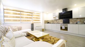 A modern living room with a sofa, a coffee table, and a kitchen area with white cabinets and a black stove. - Queen Stay Apartments (Sheffield)