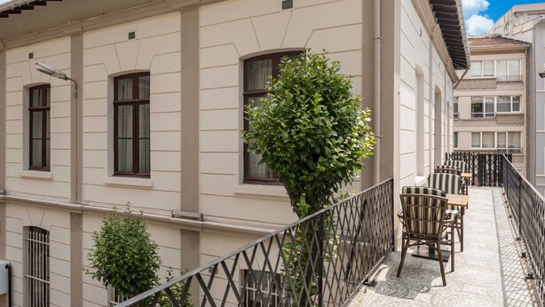 Un bâtiment doté d’un balcon, d’un espace extérieur aménagé pour s’asseoir et d’un petit arbre.