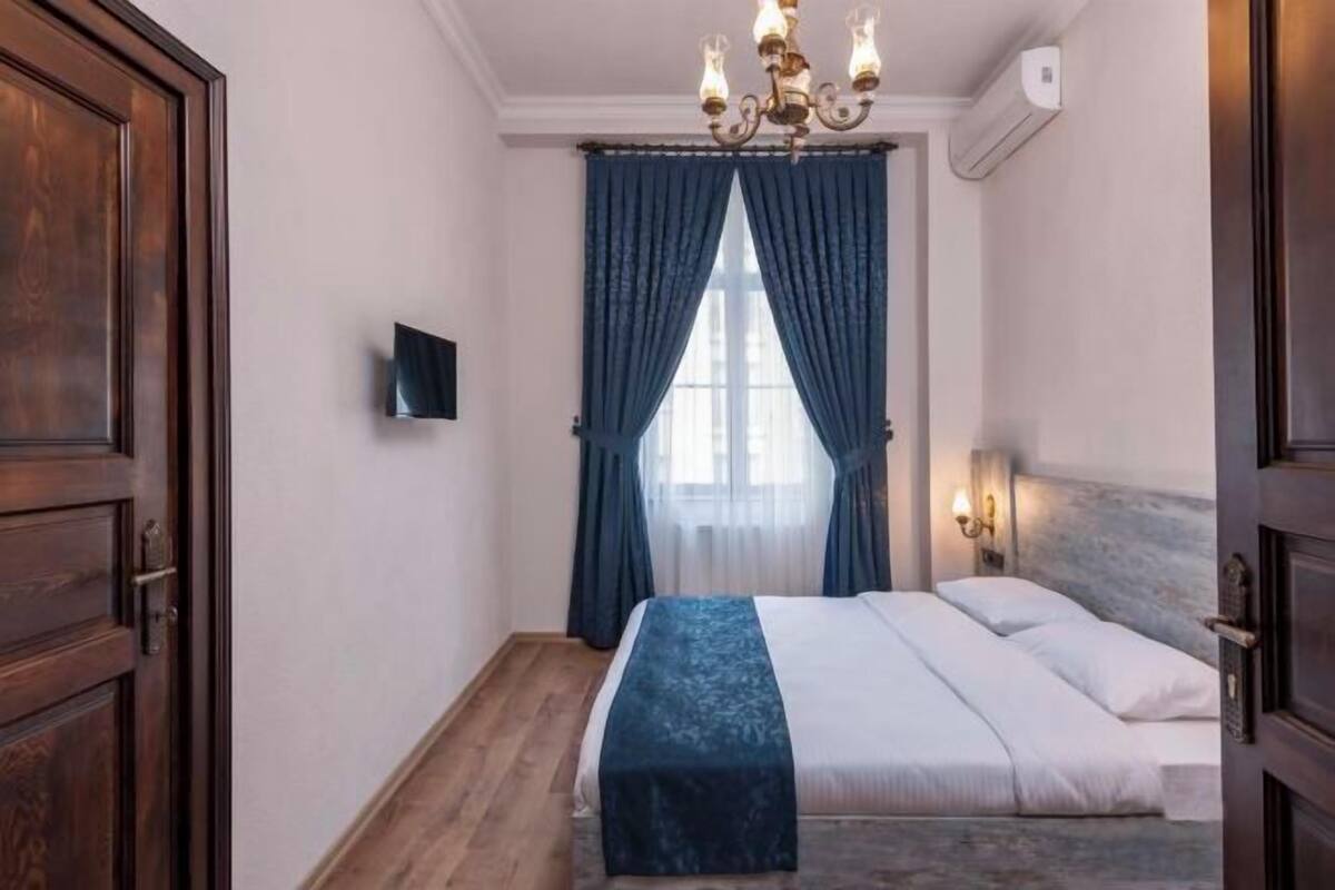A bedroom with a bed, a chandelier, a television, and a window with curtains.
