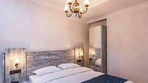 Une chambre à coucher avec un lit, des lampes de chevet, un téléphone, un lustre et un miroir.
