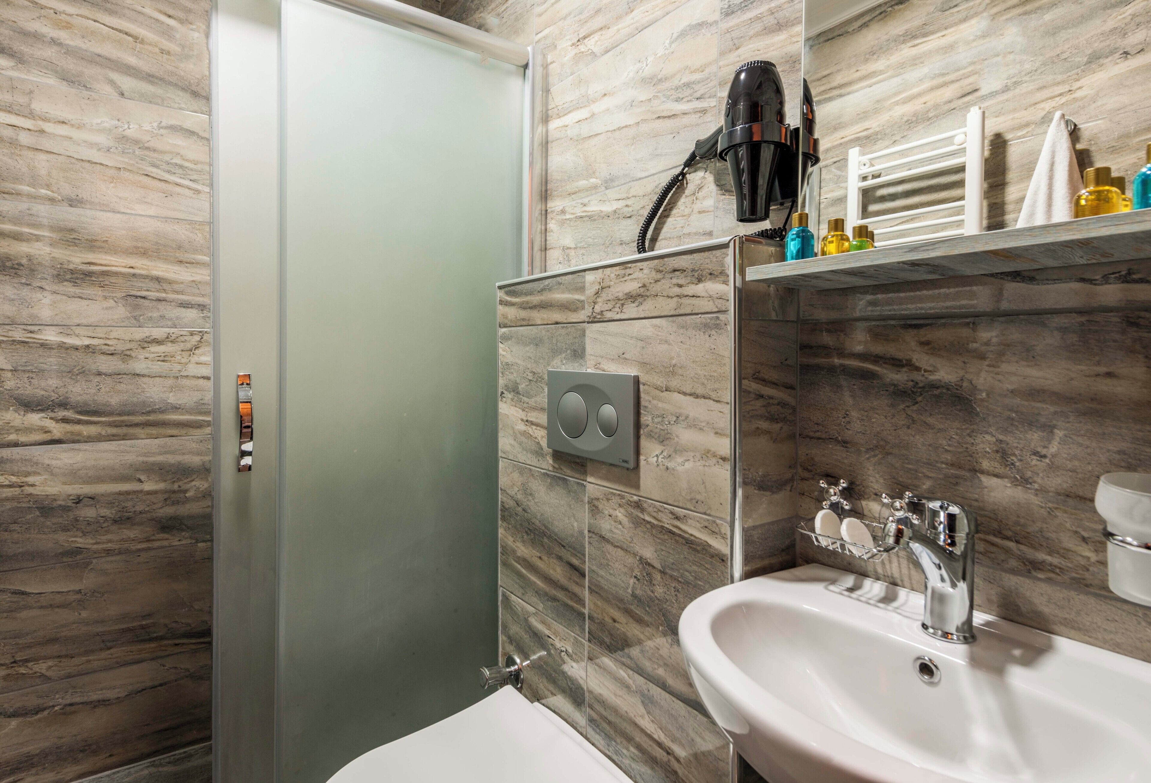 A modern bathroom with a glass shower enclosure, a white sink, and a hairdryer mounted on the wall.