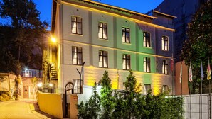 Un immeuble à plusieurs étages, doté d’une façade verte et jaune, de nombreuses fenêtres et d’une entrée bien visible, protégée par un portail en métal.