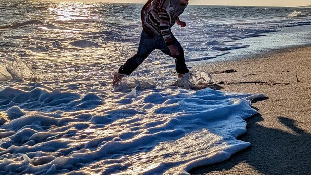 A person running along a beach with waves and the sun in the background.
