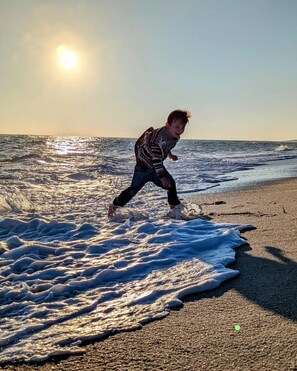 A person running along a beach with waves and the sun in the background.