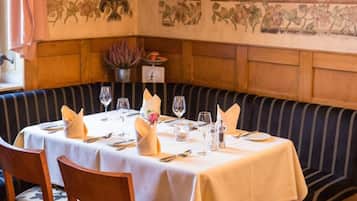 Un restaurante con una zona de asientos con bancos de madera, una mesa dispuesta con manteles blancos y un mural en la pared.
