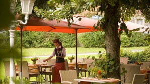 An outdoor dining area with tables and chairs, a waiter, and a large umbrella. - Hotel Eisbach (Ransbach-Baumbach)