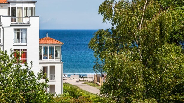 A coastal building with a balcony overlooking the sea, a pathway, and greenery. - Apartment Hotel Rosenhof (Kuehlungsborn)
