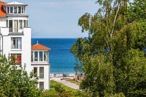 Um edifício costeiro com varanda com vista para o mar, um caminho e vegetação.