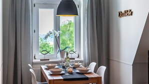 A dining area with a wooden table set for four, a black pendant light, and a window with curtains. - Apartment Hotel Rosenhof (Kuehlungsborn)