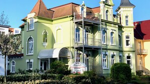A historic building with a green facade, multiple balconies, and a tower with a spire. - Apartment Hotel Rosenhof (Kuehlungsborn)
