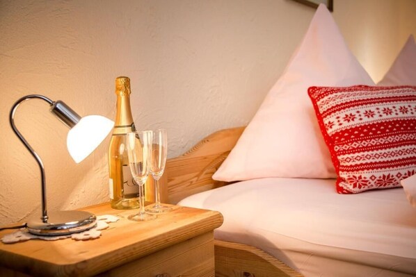 A wooden bedside table with a bottle of champagne, two glasses, and a lamp.