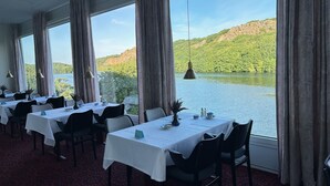 A restaurant with tables set for dining, large windows offering a view of a lake and hills. - Hotel Hammersø Apartments - Adults Only (Allinge)