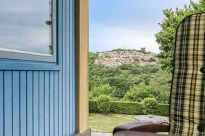 Vista dalla finestra su un edificio con esterno blu, con una collina rocciosa ricoperta di vegetazione.