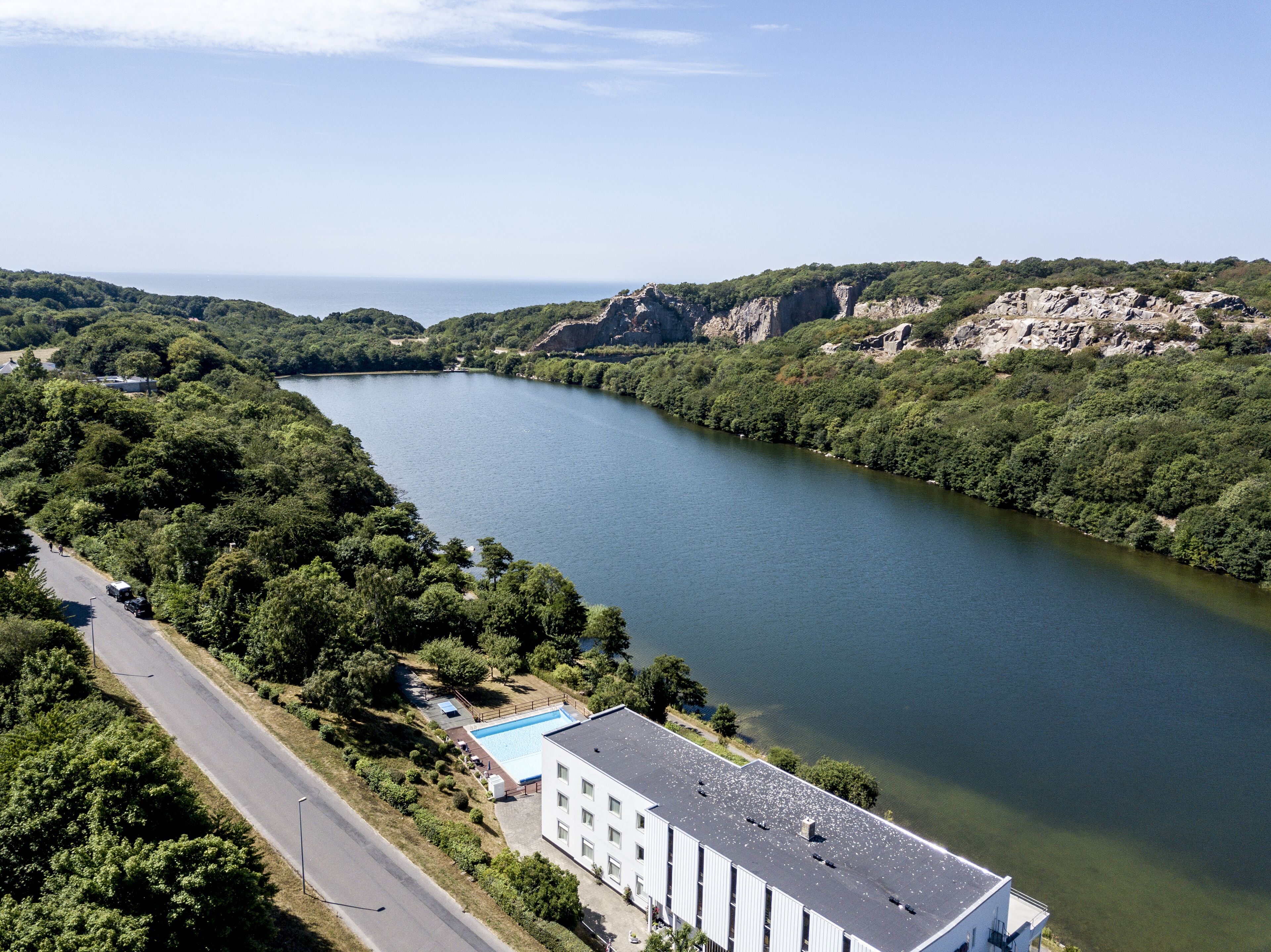 A riverside view with a building adjacent to the water, featuring a swimming pool and a parking area.