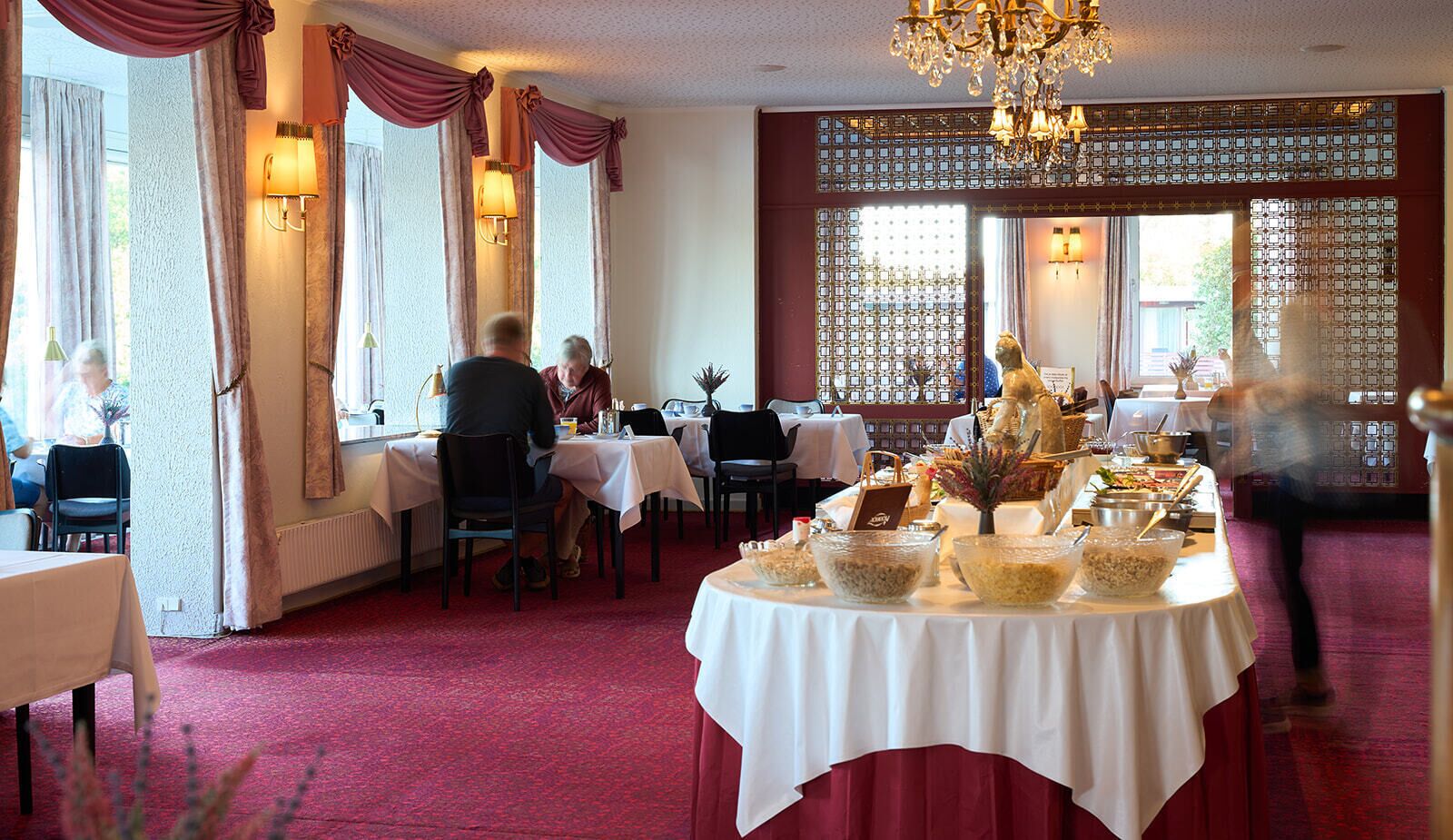 Uma sala de jantar com mesas redondas, um candelabro e um buffet.