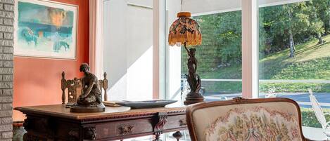 A room with a large window, a desk with a lamp, and a chair with floral upholstery.