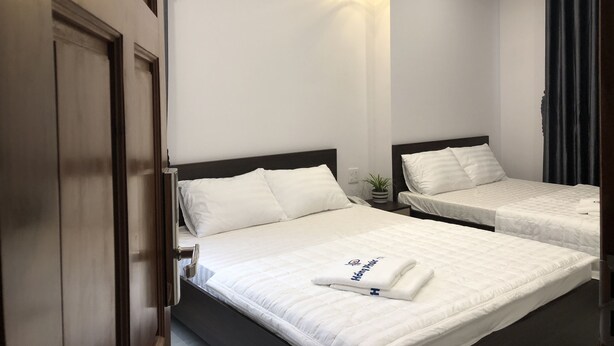 A hotel room with two single beds, a small bedside table with a lamp, and a large mirror on the wall. - Hotel Hong Phuc (Quy Nhon Nam)