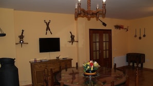Comedor con una mesa redonda de vidrio, sillas de madera, una araña, un televisor y un aparador de madera.