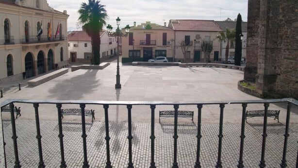 Un patio con zona pavimentada, bancos y un edificio con una torre de reloj.