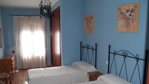 Una habitación con dos camas, un aparador de madera, un ventilador y una ventana con cortinas.