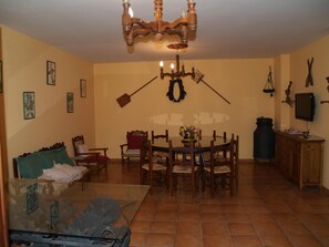 Un coin repas agrémenté d’un lustre, de chaises en bois, d’une table ornée d’un vase de fleurs et d’un téléviseur posé sur un meuble en bois.