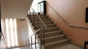 A staircase with metal railings, beige walls, and a window with blinds. - Hotel Yu (East Sarajevo)