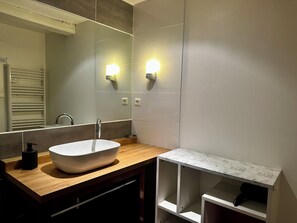 Ein modernes Badezimmer mit einem großen Spiegel, einem weißen Waschbecken und zwei Wandleuchten.
