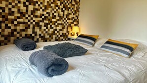 A neatly made bed with a checkered headboard, a lamp, and two patterned pillows. - Gîte Les Oliviers – 4 people – 2 bedrooms – 1 bathroom – Indoor pool (Arques)