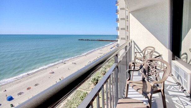 A balcony with a view of a beach and pier, featuring outdoor furniture and a railing. - Pet Friendly, Direct Oceanfront, True One Bedroom (Myrtle Beach)