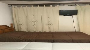 Une chambre à coucher avec un lit, une tête de lit en bois, un téléviseur fixé au mur et un rideau à motifs.