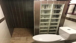 Une petite salle de bain comprenant des toilettes, un espace douche doté d’une porte en verre et des murs carrelés.