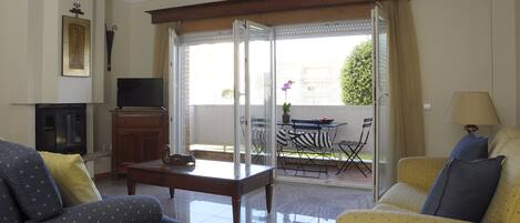 A living room with a sofa, armchair, TV, fireplace, and a view of an outdoor patio with a table and chairs.
